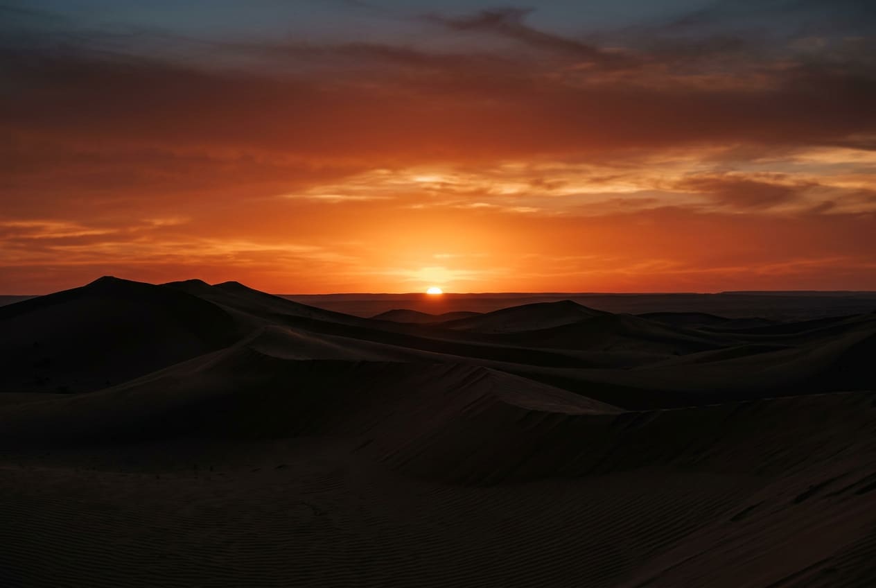 Coucher de soleil sur des dunes, ciel ambre et terracotta.